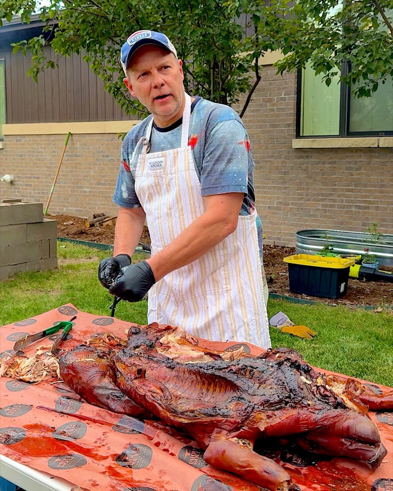 Andy Olree, founder of Rub Your Meat, carving a whole smoked pig in his backyard